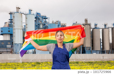 Sad young woman worker with transgender flag against background of factory Sad young woman worker with transgender flag against background of factory 101725966