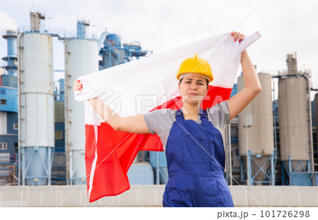Upset disappointed young female engineer in helmet waving state flag of Poland during strike in front of big tanks at chemical plant Upset disappointed young female engineer in helmet waving state flag of Poland during strike in front of big tanks at chemical plant 101726298
