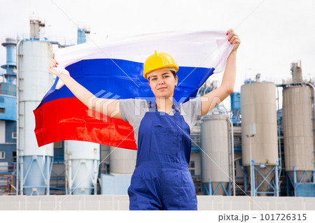 Young female engineer in helmet waving state flag of Russia while standing in front of big tanks at chemical plant Young female engineer in helmet waving state flag of Russia while standing in front of big tanks at chemical plant 101726315