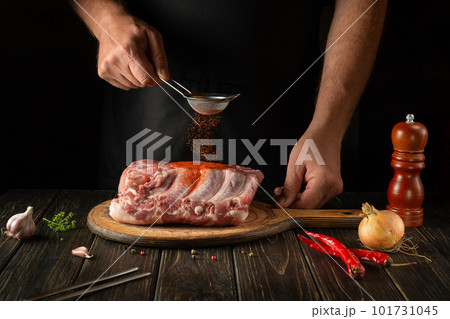 Close-up of a chef sprinkling paprika on fresh meat ribs. The concept of cooking delicious street food or grill. Black background with space for advertising Close-up of a chef sprinkling paprika on fresh meat ribs. The concept of cooking delicious street food or grill. Black background with space for advertising 101731045