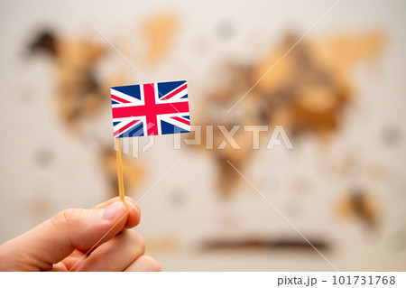 British flag in mans hand on the wooden world map background. Global economy and geopolitics concept. British flag in mans hand on the wooden world map background. Global economy and geopolitics concept. 101731768