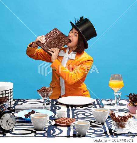 Emotionally woman in image of movie character passionately eating giant chocolate with nuts over blue background. 101740971
