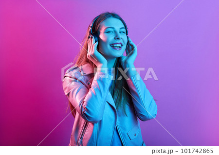 Woman listening to music on headphones enjoying favorite songs, keeps eyes closed, laughing happily, standing isolated over pink neon background. Woman listening to music on headphones enjoying favorite songs, keeps eyes closed, laughing happily, standing isolated over pink neon background. 101742865