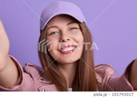 Close up portrait of cheerful tender adorable female holding photocamera, making selfie, looking directly at camera, wearing pink cap, having pleasant facial expression. Youth and tech concept. Close up portrait of cheerful tender adorable female holding photocamera, making selfie, looking directly at camera, wearing pink cap, having pleasant facial expression. Youth and tech concept. 101743017