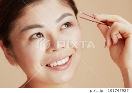 modern asian woman with tweezers on beige background 101747927