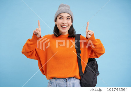 Happy korean girl points fingers up, shows advertisement, invites to click banner on top, stands over blue background Happy korean girl points fingers up, shows advertisement, invites to click banner on top, stands over blue background 101748564