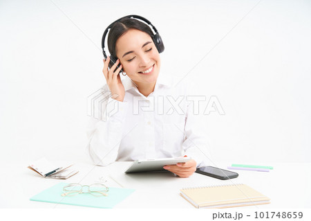 People and workplace. Smiling asian woman sits in office, student listening music in headphones and holding digital tablet, white background People and workplace. Smiling asian woman sits in office, student listening music in headphones and holding digital tablet, white background 101748659
