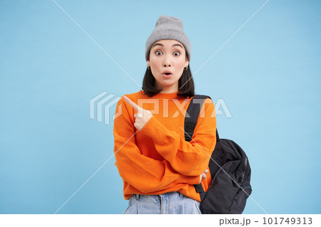 Surprised asian woman points left at smth interesting, curious about promo offer banner, blue background 101749313