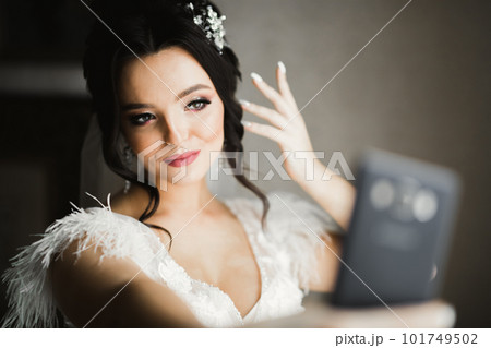 A sweet smiling bride in a light interior makes selfie on the phone 101749502