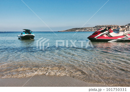A couple of recreational power jet skis with no people at the water's edge of a sandy beach shoreline in the Mediterranean sea A couple of recreational power jet skis with no people at the water's edge of a sandy beach shoreline in the Mediterranean sea 101750331