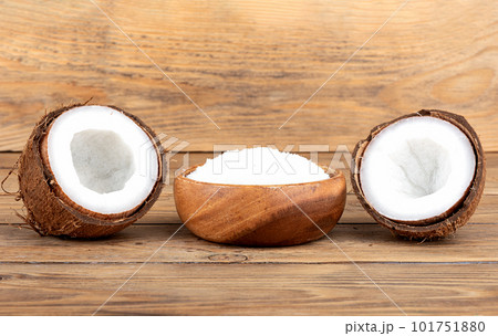 Coconut split in half and a bowl with coconut flakes on a wooden background. Coconut split in half and a bowl with coconut flakes on a wooden background. 101751880