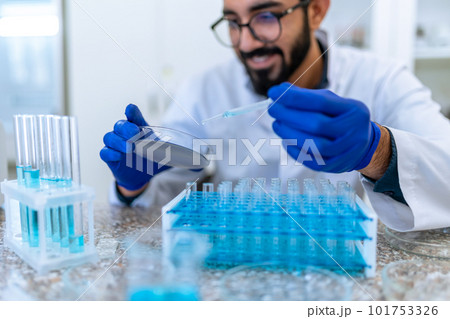 Smiling scientist man testing chemical sample in flask at laboratory with lab glassware. 101753326