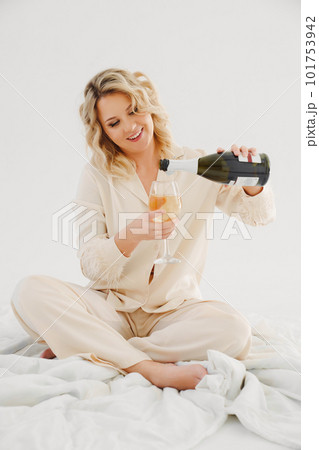 blonde in delicate pajamas in bed with a bottle and a glass of champagne blonde in delicate pajamas in bed with a bottle and a glass of champagne 101753942
