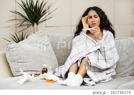 Young woman looks at the thermometer with horror. 101756174