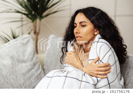 A beautiful young Arab woman escapes from the cold by wrapping herself in a blanket. The girl feels shivering and gets sick from the cold in the apartment. A beautiful young Arab woman escapes from the cold by wrapping herself in a blanket. The girl feels shivering and gets sick from the cold in the apartment. 101756176