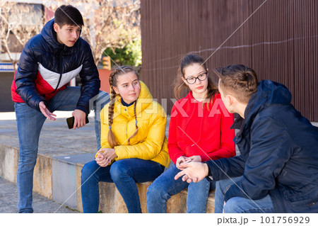 Four teenagers enthusiastically look at the screens of their smartphones on street Four teenagers enthusiastically look at the screens of their smartphones on street 101756929