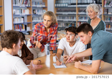 Schoolgirl talking about her favorite book. Positive teenage students and female teacher discussing in library 101757015