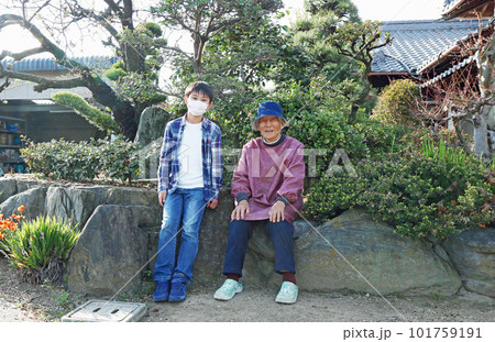 里帰りしたひ孫と曾祖母が庭で並んで座っている 101759191