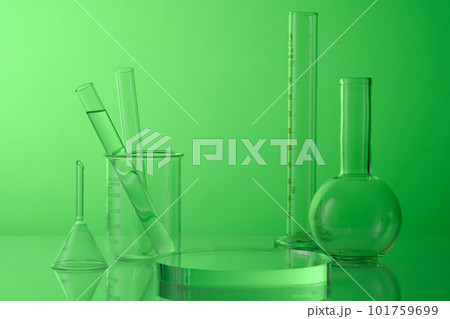 Science and medical background with lab glassware - test tubes, boiling flask, beaker and round transparent podium on green background. Blank space for product presentation. 101759699