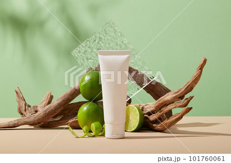 A white tube without label arranged with Lime slice and peels against pastel green background. Lime (Citrus aurantiifolia) is high in vitamin C that can help whitening skin 101760061