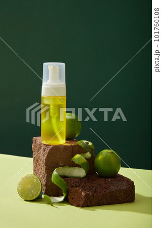 Front view of yellow spray bottle unlabeled placed on brown stone podiums and fresh limes decorated on dark background. Mockup scene for cosmetic product of lime extract. Minimal concept 101760108