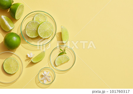 Some glass petri dishes containing white flowers and Lime slices on a light background. Empty space on the right side to show beauty product of Lime (Citrus aurantiifolia) extract 101760317