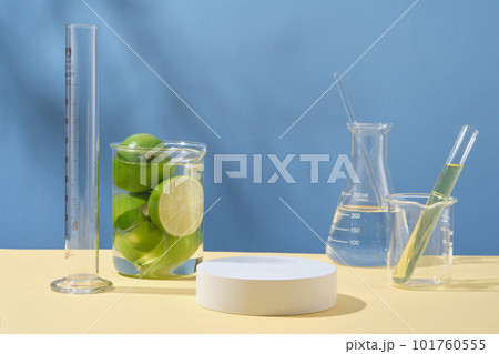 Front view of round empty podium, fresh limes and laboratory glassware containing transparent liquid on blue background. Blank space for display cosmetic of lime extract with minimal concept. 101760555