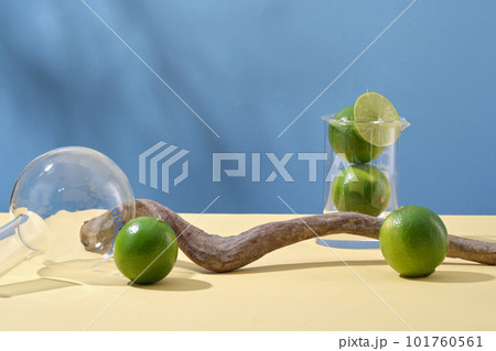 Minimal concept for display product with fresh limes, lab glassware and dried twig on blue background. Lime extract contains a lot of vitamin C and nutrients for effective skin care. 101760561