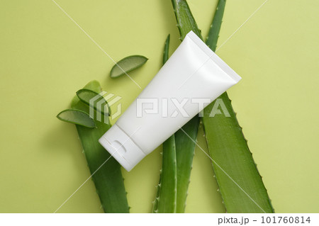 Blank label tube in white color arranged with some fresh Aloe vera slices and leaves. Aloe vera (Aloe barbadensis miller) contains polysaccharides and gibberellins, help in the growth of new cells 101760814