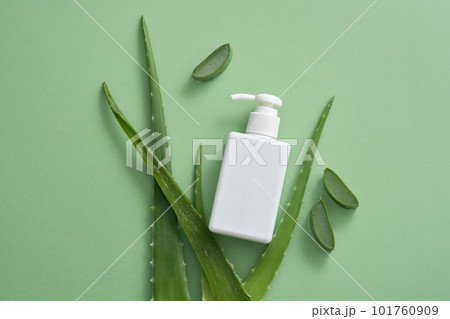 Fresh aloe vera are displayed on green background for cosmetic presentation with a white pump bottle without label. Natural extracts are used in numerous skin and hair care products. 101760909