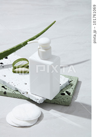 Blank plastic cosmetics container for cream or shampoo on stones podiums, makeup remover cotton and fresh aloe vera leaves decorated on white background. Cosmetic mockup extracted from aloe vera. 101761069