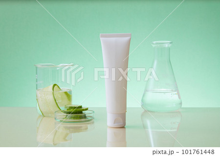 Front view of white bottle without label decorated with laboratory glassware on pastel background and cucumber slices. Research concept of cucumber extracts for cosmetics 101761448