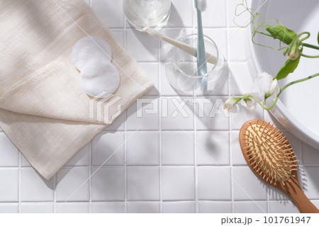 A folded towel with cotton pads, toothbrushes contained inside a glass decorated a wooden brush and white flower branches. Empty space to show your product 101761947