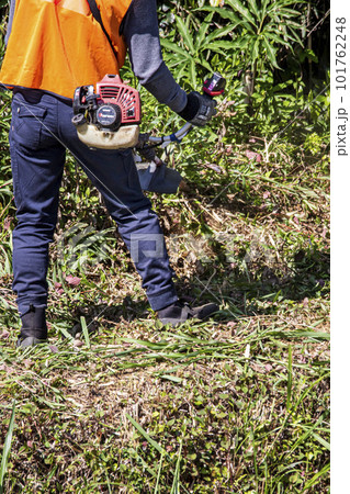 生い茂った雑草を電動草刈機で刈り込む男性植木職人 生い茂った雑草を電動草刈機で刈り込む男性植木職人 101762248