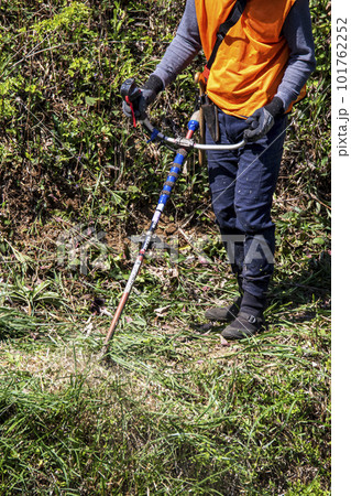 生い茂った雑草を電動草刈機で刈り込む男性植木職人 101762252