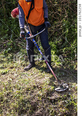 生い茂った雑草を電動草刈機で刈り込む男性植木職人 生い茂った雑草を電動草刈機で刈り込む男性植木職人 101762258