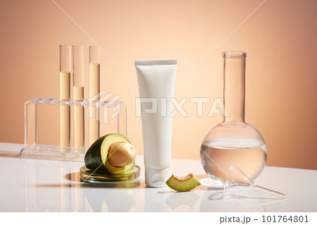 A white plastic tube unlabeled, fresh avocado slices and lab glassware decorated on pastel background. Mockup for cosmetic of avocado extract with research and development concept. A white plastic tube unlabeled, fresh avocado slices and lab glassware decorated on pastel background. Mockup for cosmetic of avocado extract with research and development concept. 101764801
