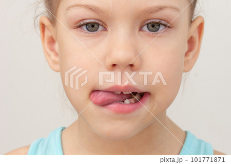 Child face with tongue out to left side cropped head caucasian little girl of 6 7 years on grey background Child face with tongue out to left side cropped head caucasian little girl of 6 7 years on grey background 101771871