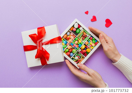 Female hands with delicious candies in box on color background Female hands with delicious candies in box on color background 101773732