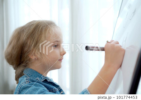 Lovely little cute girl enjoy drawing a picture and painting on a whiteboard. Elementary school age of little girl concentrate drawing on whiteboard or canvas. 101774453