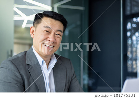 Close up portrait of successful asian financier investor, adult boss smiling and looking at camera, man working inside office at workplace with laptop. 101775331