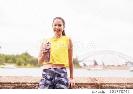 スポーツドリンクを片手にオペラハウスの前で微笑む女性 101778745