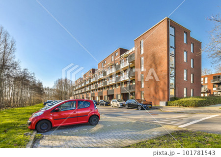 a red car parked in front of a large brick apartment building on a sunny day with blue sky and white clouds 101781543