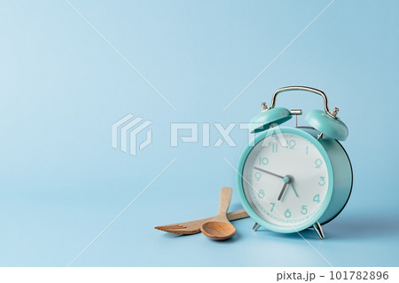 An alarm clock with cutlery set against blue background 101782896