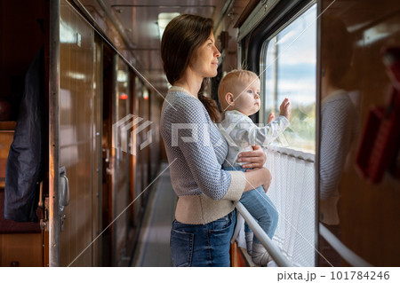 Family traveling in a train and looking through window. Mom shows his baby something outside window. Woman with child traveling by public transport. Family traveling in a train and looking through window. Mom shows his baby something outside window. Woman with child traveling by public transport. 101784246