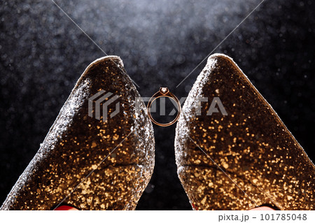 Wedding shoes and wedding rings among them. wedding ring with a diamond among two shoes on a dark background. wedding details of the bride. selective focus Wedding shoes and wedding rings among them. wedding ring with a diamond among two shoes on a dark background. wedding details of the bride. selective focus 101785048
