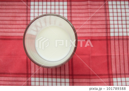 A glass of milk stands on a red checkered cloth, top view A glass of milk stands on a red checkered cloth, top view 101789388