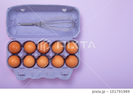 Brown raw eggs in paper tray with whisk on purrple background.Top view 101791989