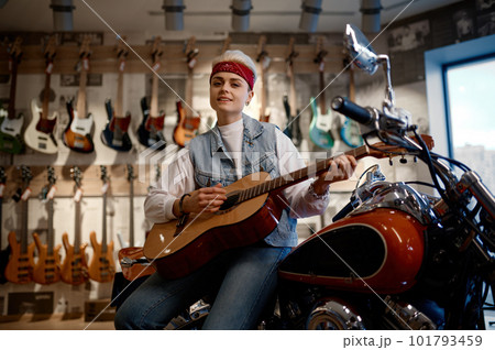 Young female rocker playing guitar at music shop sitting on motorcycle 101793459