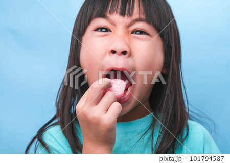Smiling cute little girl eating sweet gelatin with sugar added isolated on blue background. Children eat sugary sweets, causing loss teeth or tooth decay and unhealthy oral care. Smiling cute little girl eating sweet gelatin with sugar added isolated on blue background. Children eat sugary sweets, causing loss teeth or tooth decay and unhealthy oral care. 101794587